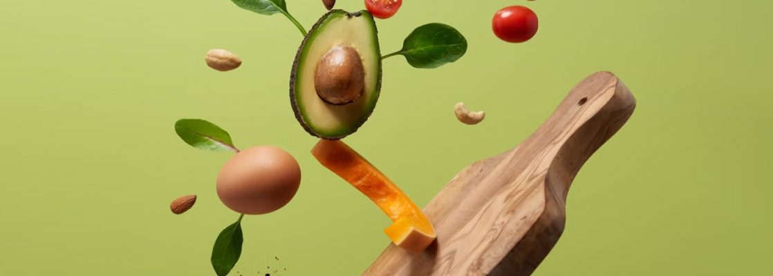 A creative arrangement of paleo diet ingredients floating above a wooden board on a green background.