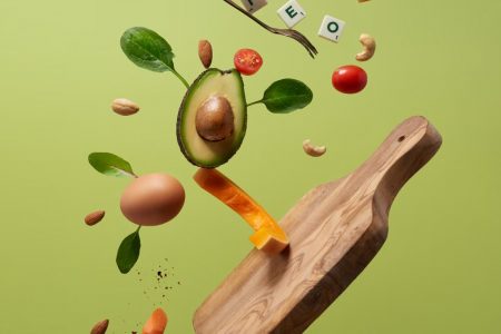 A creative arrangement of paleo diet ingredients floating above a wooden board on a green background.