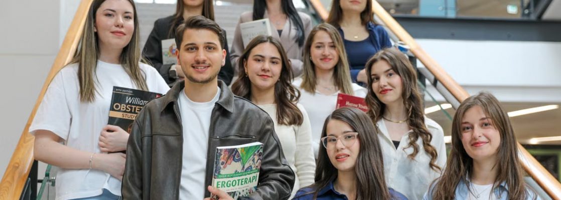 Diverse group of students smiling on stairs, holding educational books indoors.
