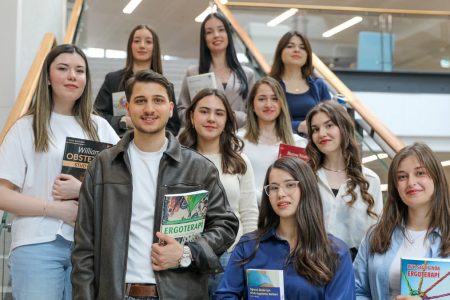 Diverse group of students smiling on stairs, holding educational books indoors.
